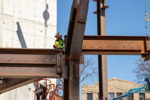 A worker aligning an overhead beam as a crane lowers it